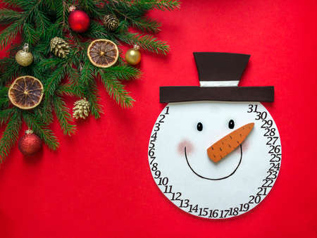 on a red background a layout in a corner of fir branches and Christmas ornaments and in the center lies the head of a snowman adventの写真素材