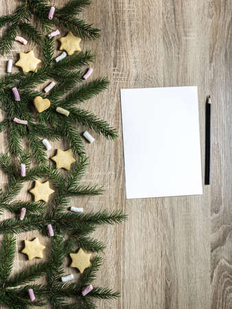 black pencil lies next to a white sheet of paper, and on the right on a wooden table are spruce branches and marshmallows, ginger biscuits in the form of asterisks and a heartの写真素材