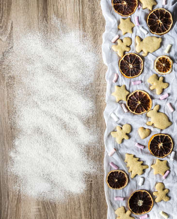 a wooden table is sprinkled with flour, and ginger spice cakes are laid out on the white cloth on the right as a tree of hearts of hares of teddy bears and stars, dried orange and marshmallow slicesの写真素材