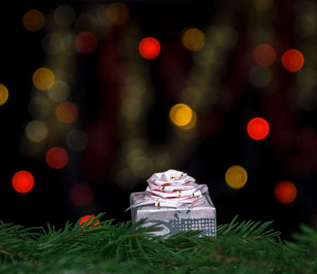 gift of pink color with a bow on fir branches against a background of yellow and red bokeh lights on a black backgroundの写真素材