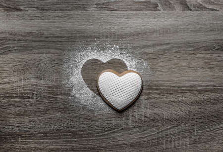 on a wooden background with powdered powder snow a silhouette of the heart is poured and below on the silhouette lies a cookie in the form of a heartの写真素材