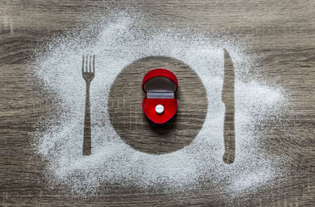 on a wooden background with powdered powder snow covered with a silhouette of a plate fork knife of appliances in the center lies a box for a ring with a white tabletの写真素材