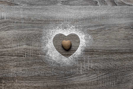 on a wooden background with powdered powder snow a silhouette of the heart is poured and in the center lies a cookie in the form of a heartの写真素材