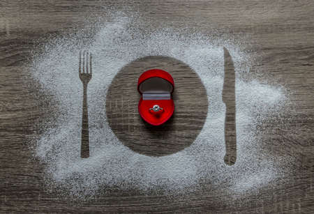 on a wooden background with powdered powder snow covered with a silhouette a plate a fork knife of appliances in the center lies a box with a ring with a diamondの写真素材