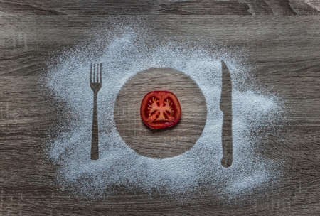 on a wooden background flour powder powdered snow silhouette plate plate fork knife appliances in the center lies a round slice of tomatoの写真素材