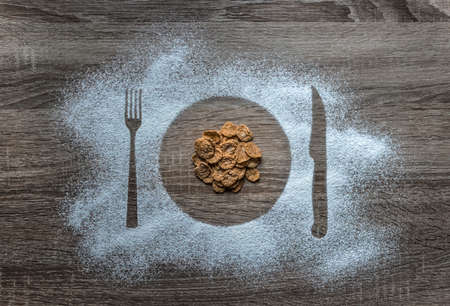 on a wooden background flour powder powdered snow silhouette plate plate fork knife appliances in the center poured corn cereal flakesの写真素材