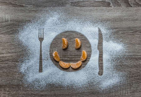 on a wooden background with powdered powder snow covered with a silhouette a plate a fork knife of appliances in the center lies a smile of orange mandarin orangeの写真素材