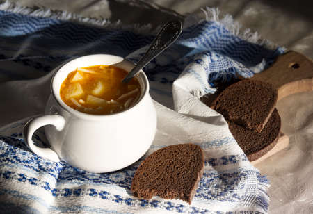 on the table a blue napkin with ornament pattern and soup tureen with yellow soup on the sun breadの写真素材