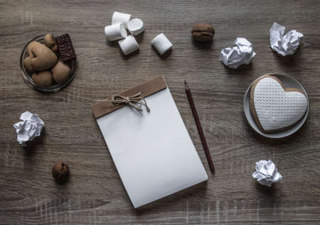 on a wooden background lies a craft notepad scrapbooking plate cookie heart pencil brown marshmallow nuts lump paper mintの写真素材
