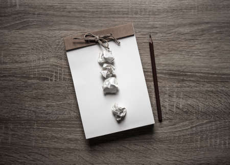 on a wooden background lies a craft notepad scrapbooking pencil on a notepad exclamation mark from crumpled paperの写真素材