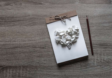 on a wooden background lies a craft notepad scrapbooking pencil on a notepad heart of crumpled paperの写真素材