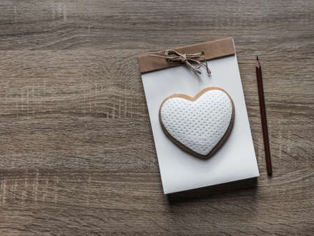 on a wooden background lies a craft notepad with a rope bow scrapbooking on it cookie heart pencil brownの写真素材