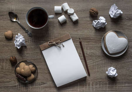 on a wooden background lies a craft notepad scrapbooking plate cookie heart pencil brown mug coffee marshmallow nuts lump paper mint spoonの写真素材