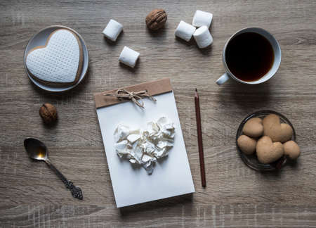 On a wooden background lies a craft notepad scrap booking plate cookie heart pencil brown mug coffee marshmallow nuts lump paper mint spoonの写真素材