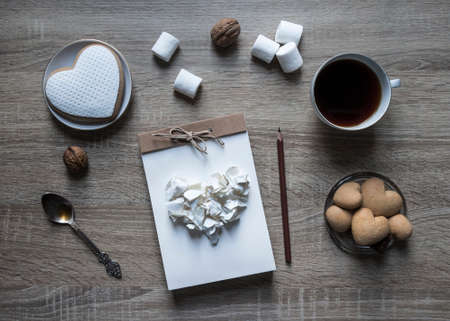 on a wooden background lies a craft notepad scrapbooking pencil on a notepad heart of crumpled paper cookies heart marshmallows nuts plateの写真素材