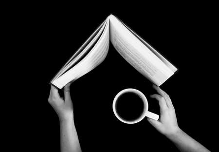 black-and-white hands hold a book and a cup with coffee top viewの写真素材