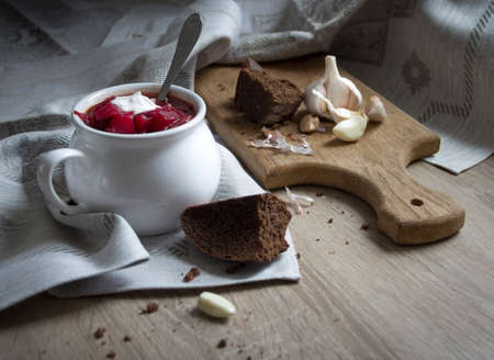 on the table a blue napkin with ornament pattern and soup tureen with red beet soup on the sun bread garlic sour creamの写真素材