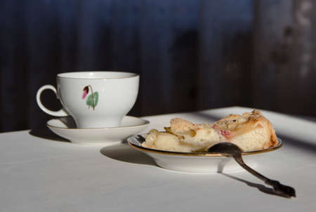 on the table a plate with a piece of apple pie, a spoon and a cup in the sunbeamの写真素材