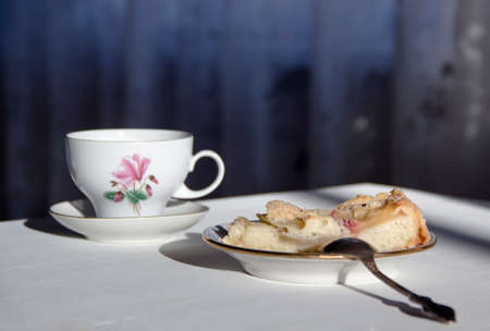 on the table a plate with a piece of apple pie, a spoon and a cup in the sunbeamの写真素材