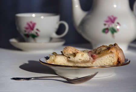 on the table a plate with a piece of apple pie, a spoon and a cup in the sunbeamの写真素材