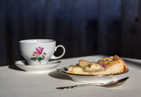 on the table a plate with a piece of apple pie, a spoon and a cup in the sunbeamの写真素材