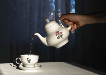 The hand holds the kettle and pours the tea in a cup in the sunlightの写真素材