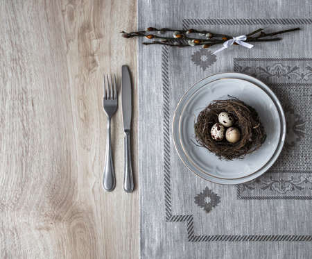 On a table a napkin with a plate a fork knife a nest with an egg of a willow twigの写真素材