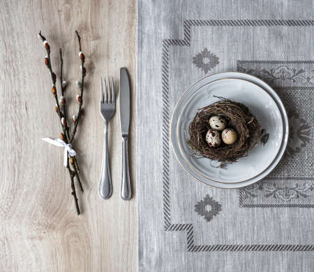 on a table a napkin with a plate a fork knife a nest with an egg of a willow twigの写真素材