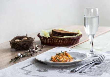 on a table a napkin with a plate of vegetable stew a glass of fork and a branch of a willow's nest with quail eggsの写真素材