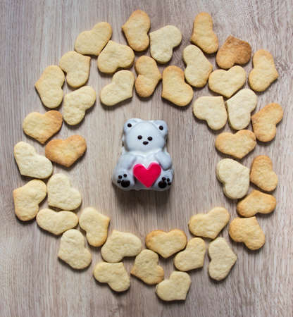 on a wooden background in a circle lie gingerbread cookies in the shape of a heart in the center lies a cake in the shape of a bear with a heart in his handsの写真素材