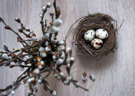 on a wooden table is a nest with eggs and a vase with willow branchesの写真素材