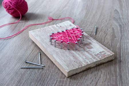 on a wooden table lay the hammer nails thread pink and gift with their own hands the heart of thread and nailsの写真素材