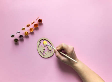 on a pink background of paint red and orange color hand with a brush paints a wooden billet egg...