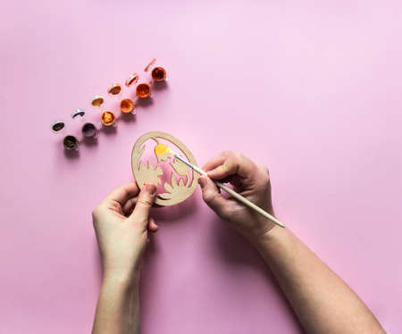 on a pink background of paint red and orange color hand with a brush paints a wooden billet egg flowers tulip narcissusの写真素材