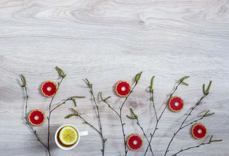 on a wooden background of a birch branch with blossoming buds of green buds and a red biscuit a cup of tea with lemonの写真素材
