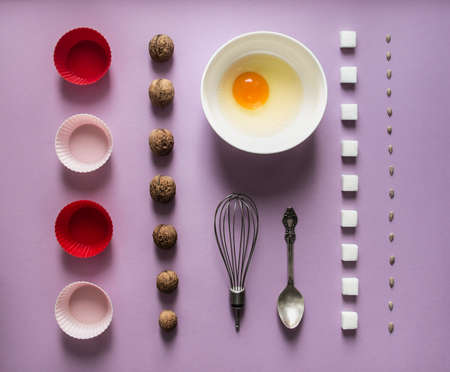 Flat lay of walnuts, sunflower seeds sunflower, sugar cubes, egg and cupcake mold with whisk and spoonの写真素材