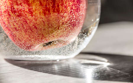 apple red orange yellow in a vase with water in air bubbles horizontal on the table flare close-up macroの写真素材