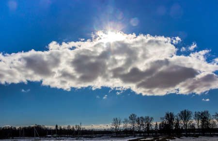 on a blue sky clouds on a diagonal horizontal sun bright glare beams expanse treesの写真素材