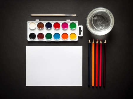 on a dark paint background brush pencils colored water sheet paper horisontal top view flat lay knollingの写真素材