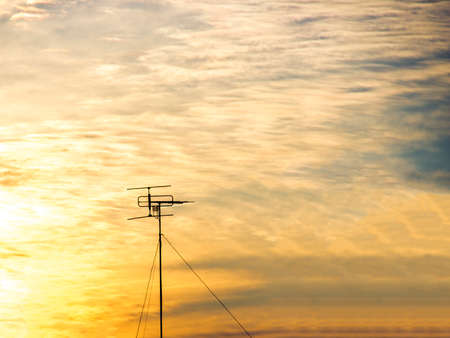 TV antenna on the background of the setting sun with yellow clouds light streamingの写真素材