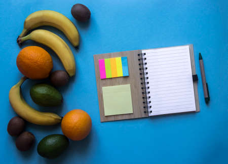 on a blue background notebook on springs notes stickers colored pen lie fruit oranges bananas avocado kiwiの写真素材
