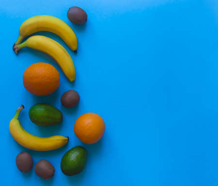 on a blue background on the side lie fruit oranges bananas avocado kiwiの写真素材