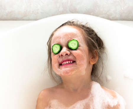 a girl smiles a snow-white smile lies in a bathroom face is smeared with cream white cream in front of a cucumberの写真素材