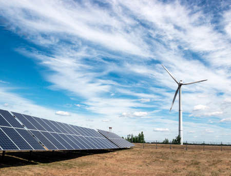 wind generator of electricity from three blades and solar panel batteries of photocells against a background of clouds and blue skyの写真素材