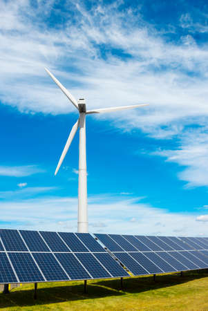 wind generator of electricity from three blades and solar panels of a battery of photocells against a background of clouds and a blue sky green grassの写真素材