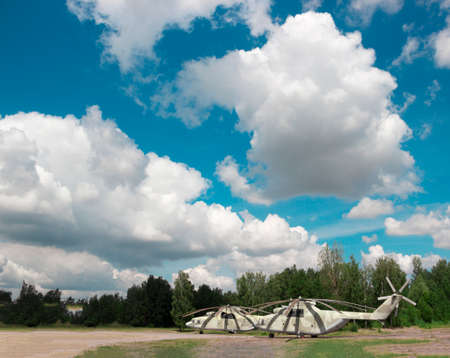 two large helicopters stand on the grass near the forest in the background of a beautiful blue sky with cloudsの写真素材