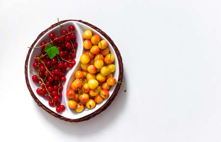 on white background round bowl of yin yang with summer berries of red currant and yellow cherry green leafの写真素材