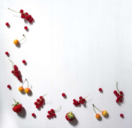 on a white background frame with the edge and from below lie berries and twigs currant red strawberry cherry white pattern copy spaceの写真素材