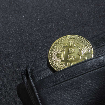 on a black background with a bokeh with sequins is a black leather wallet purse for money with a coin of crypto currency currency bitcoinの写真素材