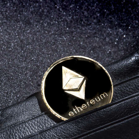 on a black background with a bokeh with sequins is a black leather wallet purse for money with a coin of the crypto currency currency ethereumの写真素材